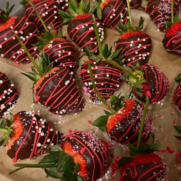 Chocolate-dipped strawberries with pink and white sprinkles on a brown surface.