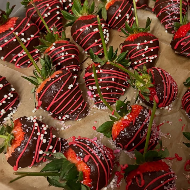 Chocolate-dipped strawberries with pink and white sprinkles on a brown surface.