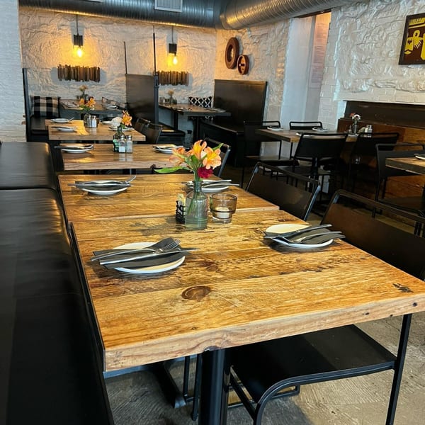 Interior of Wicked Sisters restaurant with wooden tables, black booths, and exposed brick walls.