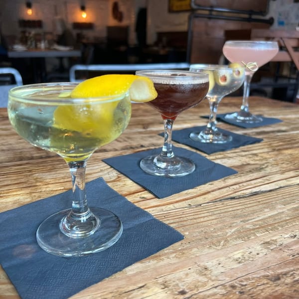 Four cocktails, including a martini with a lemon twist, on a wooden table at Wicked Sisters.