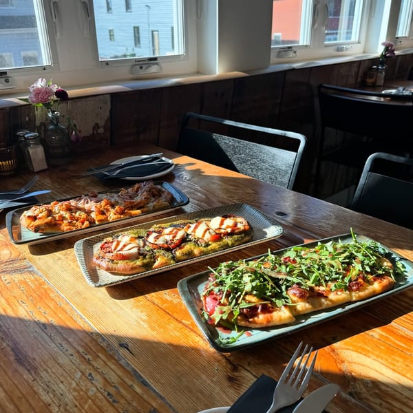 Three flatbreads with various toppings, including pesto, mozzarella, and arugula, on a wooden table.