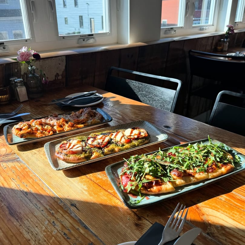 Three flatbreads with various toppings, including pesto, mozzarella, and arugula, on a wooden table.