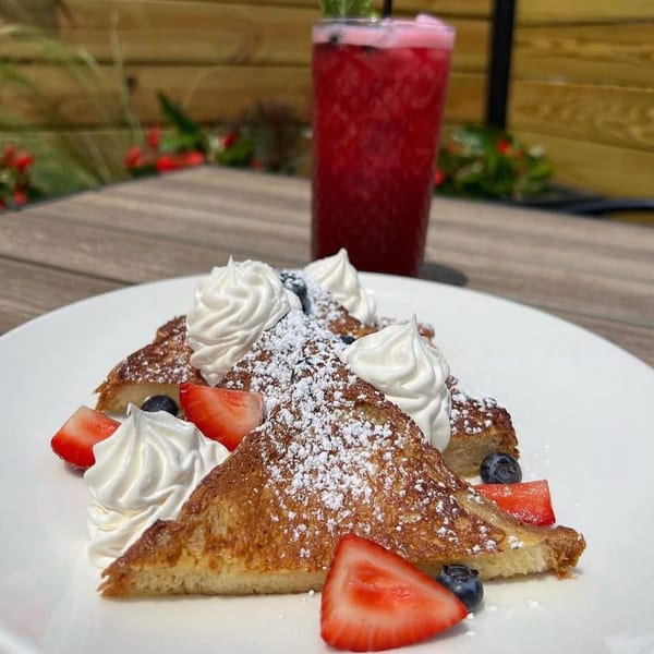 Wicked Sisters' French toast with whipped cream, strawberries, blueberries, and powdered sugar, with a red drink.