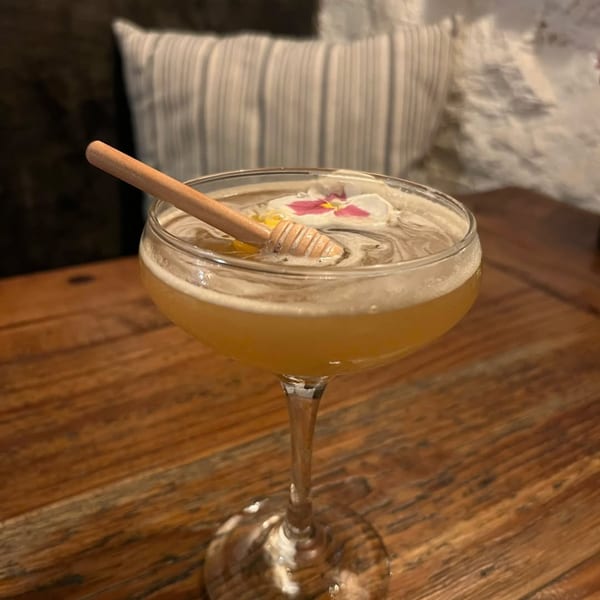 Honey-colored cocktail with a honey dipper and edible flowers on a rustic wooden table.