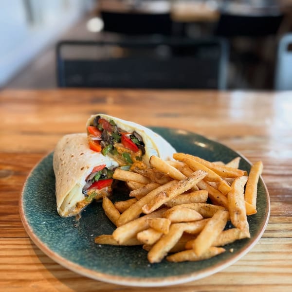 A Wicked Sisters' wrap filled with vegetables and sauce, served with a side of golden fries.