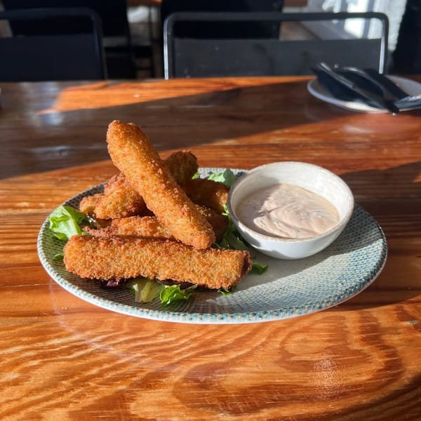 Crispy fried mozzarella sticks with a side of dipping sauce on a rustic wooden table at Wicked Sisters.