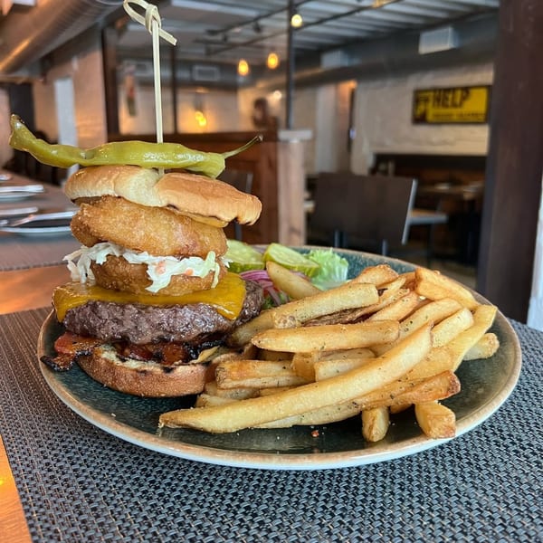 A Wicked Sisters burger with onion rings, coleslaw, cheese, and a side of fries and pickles.