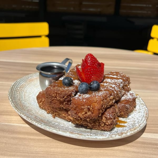 Crispy French toast sticks with powdered sugar, caramel, blueberries, and a carved strawberry on a plate.