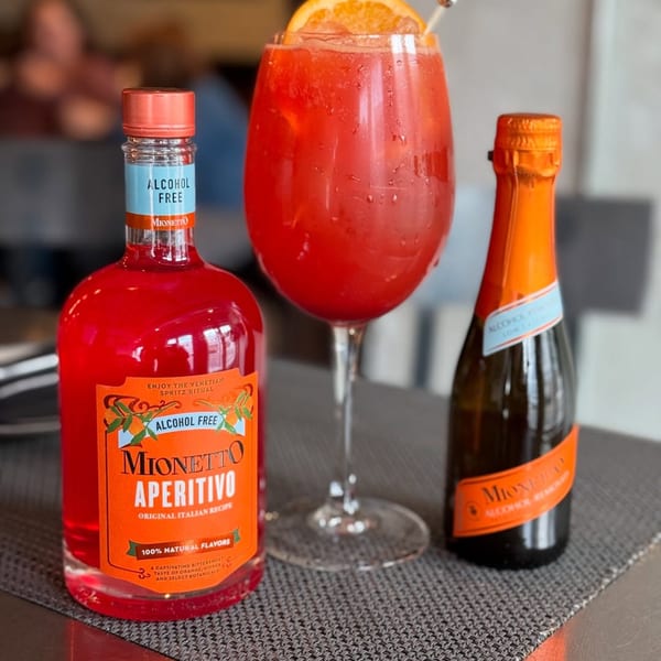 A vibrant red Aperitivo cocktail with an orange slice, alongside bottles of Mionetto Aperitivo and sparkling wine.